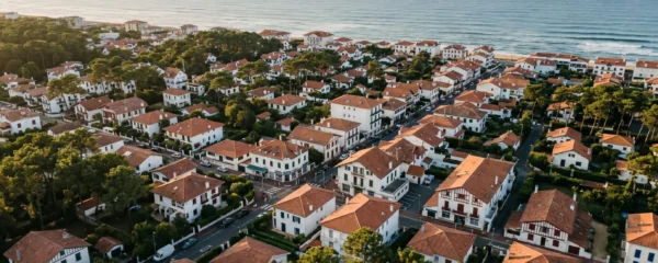 Vue aérienne du centre d'Hossegor avec ses villas balnéaires à toits rouges, pins maritimes et l'océan Atlantique en arrière-plan, illustrant la densité urbaine et l'attractivité du marché immobilier côtier landais